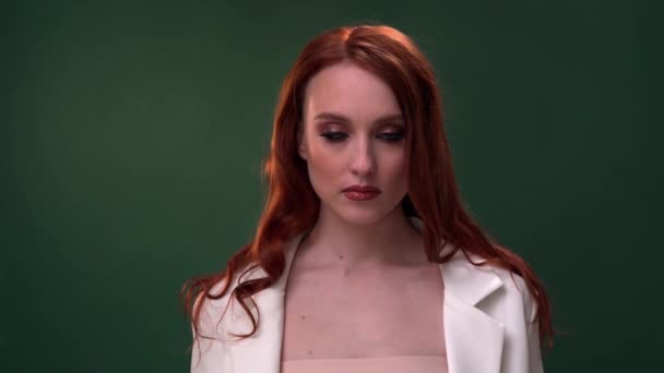 Mooi modieus meisje met lang krullend rood haar. Meisje in de studio met een groene achtergrond. Reclame, haarproducten, schoonheidssalon, cosmetica, kleding. Mode, boetiek. — Stockvideo