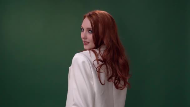 Красивая модная девушка с длинными вьющимися рыжими волосами. Девушка в студии на зеленом фоне. Реклама, средства для волос, салон красоты, косметика, одежда. Мода, бутик. — стоковое видео
