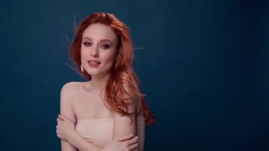 Uzun kıvırcık kızıl saçlı güzel, modaya uygun bir kız. Stüdyoda mavi arka planda bir kız var. Reklamlar, saç ürünleri, güzellik salonu, kozmetik ürünleri, kıyafetler. Moda, butik.