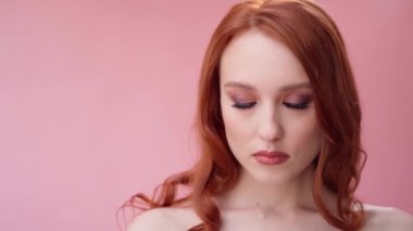 Uzun kıvırcık kızıl saçlı güzel, modaya uygun bir kız. Stüdyoda pembe arka planda bir kız var. Reklamlar, saç ürünleri, güzellik salonu, kozmetik ürünleri, kıyafetler. Moda, butik. Pembe..