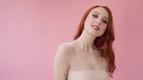 Vacker fashionabel flicka med långt lockigt rött hår. Flicka i studion på en rosa bakgrund. Reklam, hårprodukter, skönhetssalong, kosmetika, kläder. Mode, butik. Pink. — Stockvideo