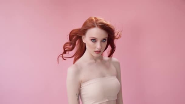 Красивая модная девушка с длинными вьющимися рыжими волосами. Девушка в студии на розовом фоне. Реклама, средства для волос, салон красоты, косметика, одежда. Мода, бутик. Розовый. — стоковое видео