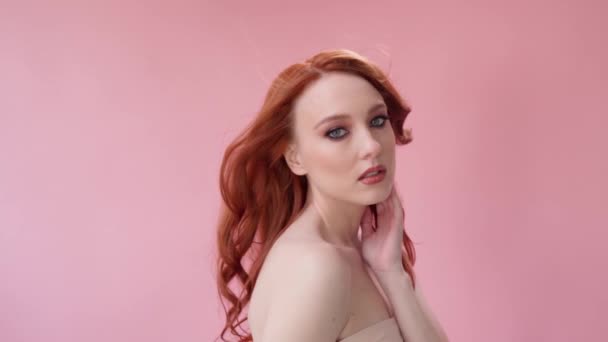Красивая модная девушка с длинными вьющимися рыжими волосами. Девушка в студии на розовом фоне. Реклама, средства для волос, салон красоты, косметика, одежда. Мода, бутик. Розовый. — стоковое видео