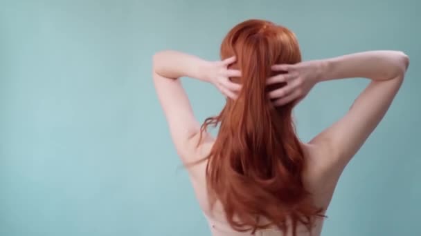 Красивая модная девушка с длинными вьющимися рыжими волосами. Девушка в студии на синем фоне. Реклама, средства для волос, салон красоты, косметика, одежда. Мода, бутик. — стоковое видео