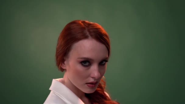 Vacker fashionabel flicka med långt lockigt rött hår. Flicka i studion på en grön bakgrund. Reklam, hårprodukter, skönhetssalong, kosmetika, kläder. Mode, butik. — Stockvideo