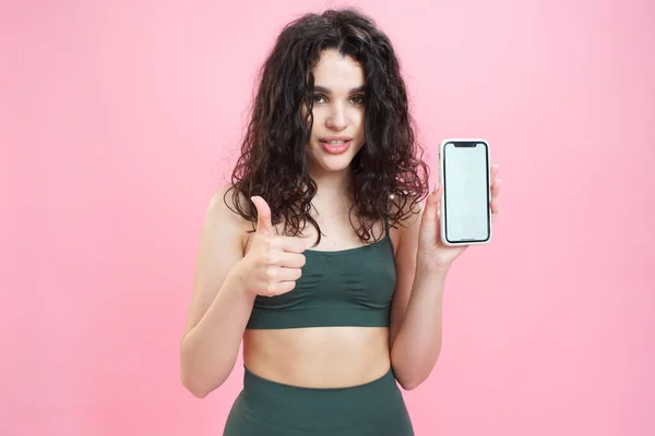 Sporty girl advertises fitness mobile app on pink background. Stock Picture