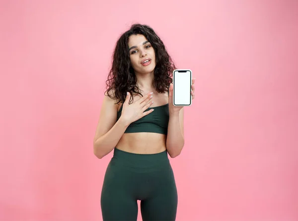 Sportief meisje adverteert fitness mobiele app op roze achtergrond. Stockafbeelding