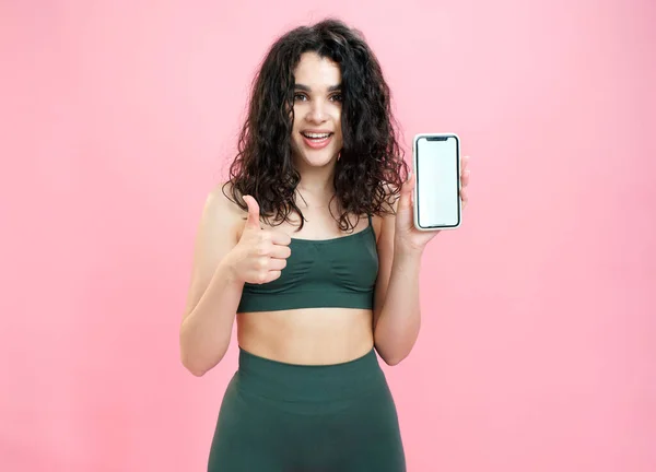 Sporty girl fait la publicité de fitness application mobile sur fond rose. Images De Stock Libres De Droits