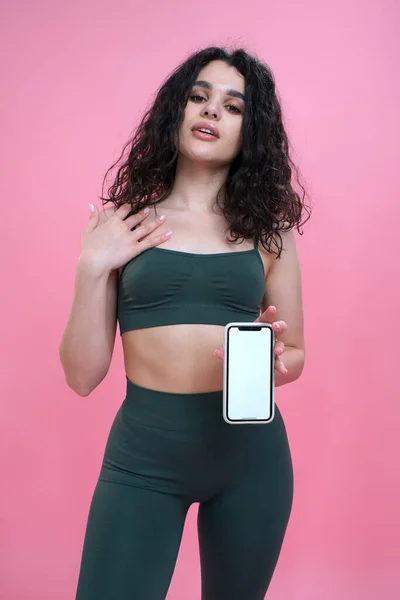 Sporty girl advertises fitness mobile app on pink background. Stock Photo