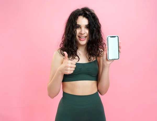 Sporty girl advertises fitness mobile app on pink background. Stock Picture