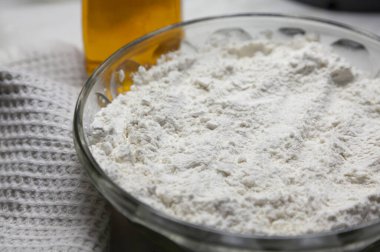 Bowl with flour on the background of a bottle of oil. Macro