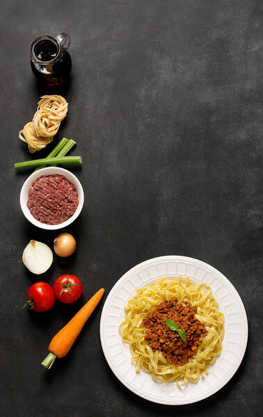 Спагетти болоньезе и его ингредиенты на черном фоне
