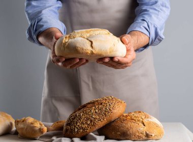 Fırıncı gri arka planda taze pişmiş ekmek tutuyor.