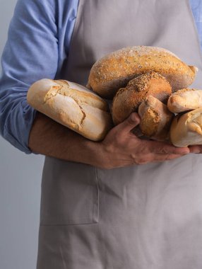 Önlüklü fırıncı gri arka planda taze pişmiş ekmeği masanın üzerinde tutuyor.