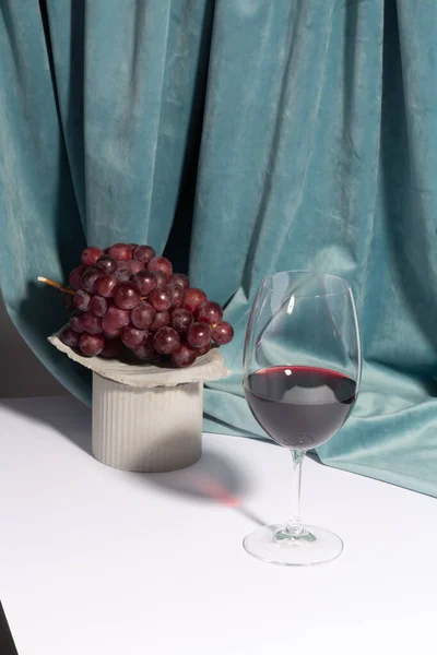 Weinglas Und Trauben Auf Betonpodest Vor Weißem Hintergrund Mit Vorhang — Stockfoto