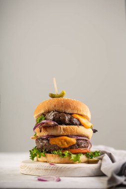 İki pirzolalı ev yapımı burger ve üzerine soğan ve salatalık soslu erimiş peynir.