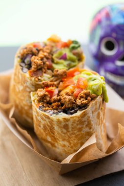 Fast food caddesindeki bir kafede kıyma ve salsa soslu burrito ve arka planda kafatası ile guacamole. Geleneksel Meksika yemeği