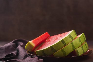 Koyu arkaplanda büyük kırmızı çiğ karpuz parçaları. Tatlı, sulu bir et, genellikle koyu kırmızıdan pembeye, bir sürü siyah tohumla, çekirdeksiz türler olmasına rağmen.