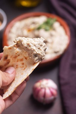Erkek ellerinin Pita ekmeğine bulaşmış Levantine mutfağı aperatifleri Baba ganoush, Ezme bir tabak sarımsağın arka planında