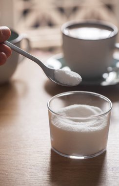 Kahve arka planında kasenin üzerinde tatlandırıcı ile kaşık tutan bir erkek.