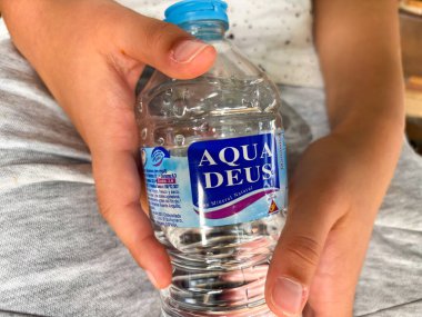 Alicante, İspanya - 15 Ekim 2025: Bir çocuk bir şişe Aqua Deus maden suyu tutuyor, açık hava ortamında suyun önemini vurguluyor