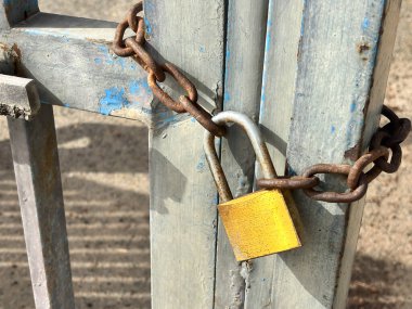 Alicante, İspanya - 15 Ekim 2025: Sarı asma kilit paslı bir zincire sahip eskimiş mavi bir kapıyı emniyete alıyor.