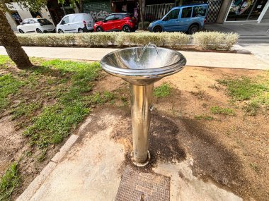 Alicante, İspanya - 15 Ekim 2025: Otoparkta çevresi çimenler ve park edilmiş araçlarla çevrili olan şehir içme havuzu, yoldan geçenlere içecek bir şeyler sunuyor