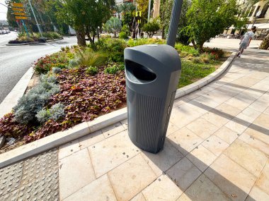 Alicante, İspanya - 15 Ekim 2025: Renkli bitkilerin arasında yer alan ve temiz bir kentsel çevreye katkıda bulunan çağdaş çöp kutusu