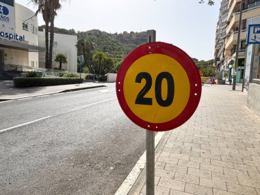 Alicante, İspanya - 15 Ekim 2025: Hız limiti işareti, arka planda palmiye ağaçları ve binaları bulunan huzurlu bir caddede saatte 20 km hız gösteriyor