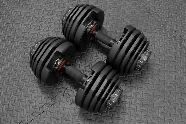 Adjustable weight dumbbell in plastic polymer material on black rubber floor.Users can choose the weight of the exercise program as needed for bodybuilding.