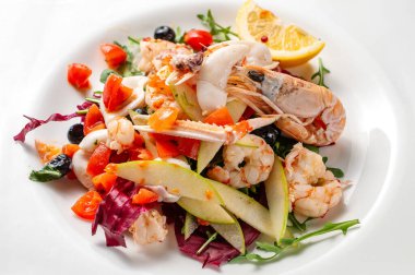 Karides, mürekkep balığı, karides, yengeç, yengeç ve sebze karışımından oluşan taze Akdeniz yemekleri beyaz bir tabakta servis edilir..