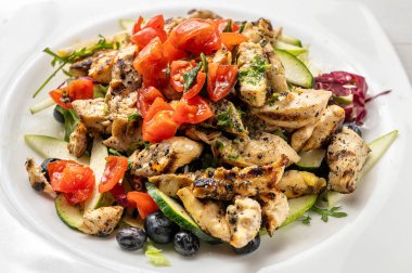 Beyaz bir tabakta taze sebze ve zeytin ile servis edilen ızgara tavuk göğsü içeren sağlıklı Akdeniz yemeği.