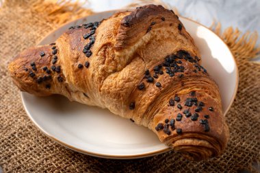 Kırsal bir arka planda seramik tabakta servis edilen çikolata parçalı gevrek kruvasan.