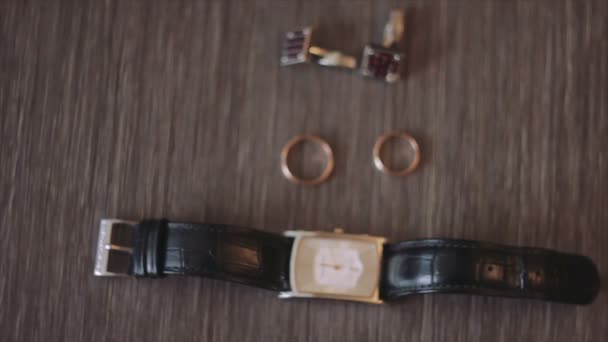 Наручные часы, кольца и два шипа на столе — стоковое видео