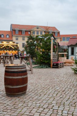 Tahta masalar, köknar ağaçları ve Wolfenbuettel 'deki Noel pazarında festival ışıkları, 25 Kasım 2025' te saat 15: 27 'de çekildi. Süslemeler arasında gezen ziyaretçiler