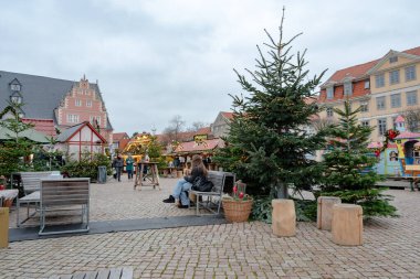 Ziyaretçiler, Wolfenbuettel 'deki Noel pazarında süslenmiş tezgahların arasında yürürken, 25 Kasım 2025' te saat 15: 45 'te fotoğraflandı. Ağaçlar ve ışıklandırma sahneyi şekillendirir.