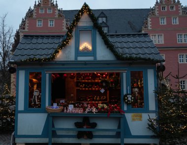 25 Kasım 2025 'te saat 16: 27' de Wolfenbuettel 'deki Noel pazarında çelenkler, mumlar ve süslemelerle süslenmiş bir tezgah fotoğrafı çekildi. Işıklar ve köknar ağaçları sahneyi oluşturur.