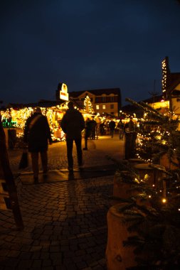 Wolfenbuettel 'deki Noel pazarında 25 Kasım 2025' te saat 17: 13 'te, yoldan geçenlerin bulanık, sıcak sicim ışıkları ve süslü tezgahlarla çekilmiş akşam sahnesi.. 