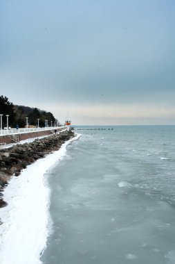 Kısmen donmuş Baltık Denizi boyunca uzanan karla kaplı bir gezinti güvertesi. Kış kıyı şeridi boyunca uzanan kavisli buz şeridi güçlü bir dikey bileşime sahiptir..