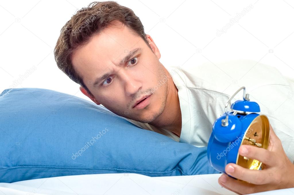 Overslept man looking at blue alarm clock horrified