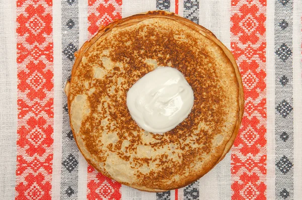 Pannenkoeken en zure room op tafelkleed met patronen, bovenaanzicht Stockfoto