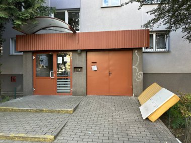 Varşova, Polonya - 24 Eylül 2025: Turuncu kapılı ve tenteli modern konut girişi, kaldırıma atılmış mobilyalar, kentsel yaşam tarzı ve toplum yaşam tarzını yansıtıyor