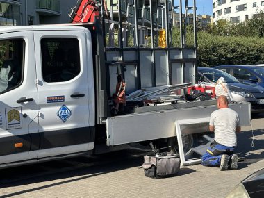 Varşova, Polonya - 24 Eylül 2025: İnşaat işçisi iş kamyonuyla diz çöktü, kentsel bir ortamda alet ve malzemelerle ekipman tamir etmeye odaklandı
