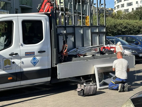 Varşova, Polonya - 24 Eylül 2025: İnşaat işçisi iş kamyonuyla diz çöktü, kentsel bir ortamda alet ve malzemelerle ekipman tamir etmeye odaklandı