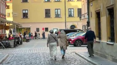 Varşova, Polonya - 3 Eylül 2025: İki yaşlı kadın şehrin canlı atmosferinin tadını çıkararak kaldırım taşı caddesinde birlikte yürüyor, kamera hareketlerini izliyor