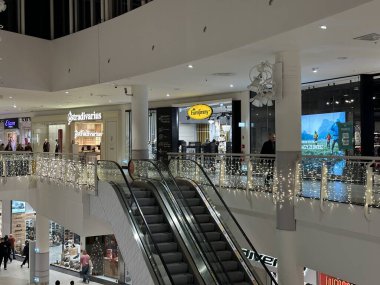 Varşova, Polonya - 20 Kasım 2025: Noel ışıkları ve dekorasyonlarla süslenmiş alışveriş merkezi, canlı bir tatil ortamında yürüyen merdivenler ve perakende satış mağazaları