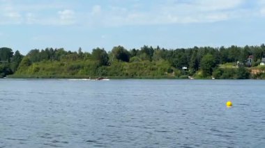 Canlı yeşillik ve uzak bir kıyı şeridi ile çerçevelenmiş sakin su üzerinde zarif bir şekilde hareket eden bir tekne, doğanın güzelliğini pürüzsüz bir kamera zoom 'uyla sergiliyor.