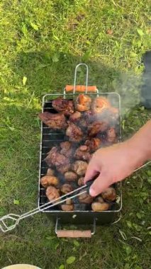 Portatif bir barbeküde marine edilmiş et ve mantar ızgarası pişirme işlemini duman ve canlı renklerle, kamera tavalarıyla ve vurgu için yakınlaştırma