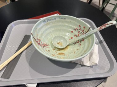 Kiraz çiçeği desenli dekoratif ramen kasesi tepside yemek çubukları ve kaşığın yanında boş oturur ve doyurucu bir yemek deneyimini ön plana çıkarır.