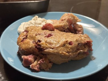 Mavi bir tabakta karışık böğürtlenli fırında tatlı, kremalı süsleme ile birlikte, paylaşım ve keyif için hoş ve davetkar bir atmosfer yaratıyor.